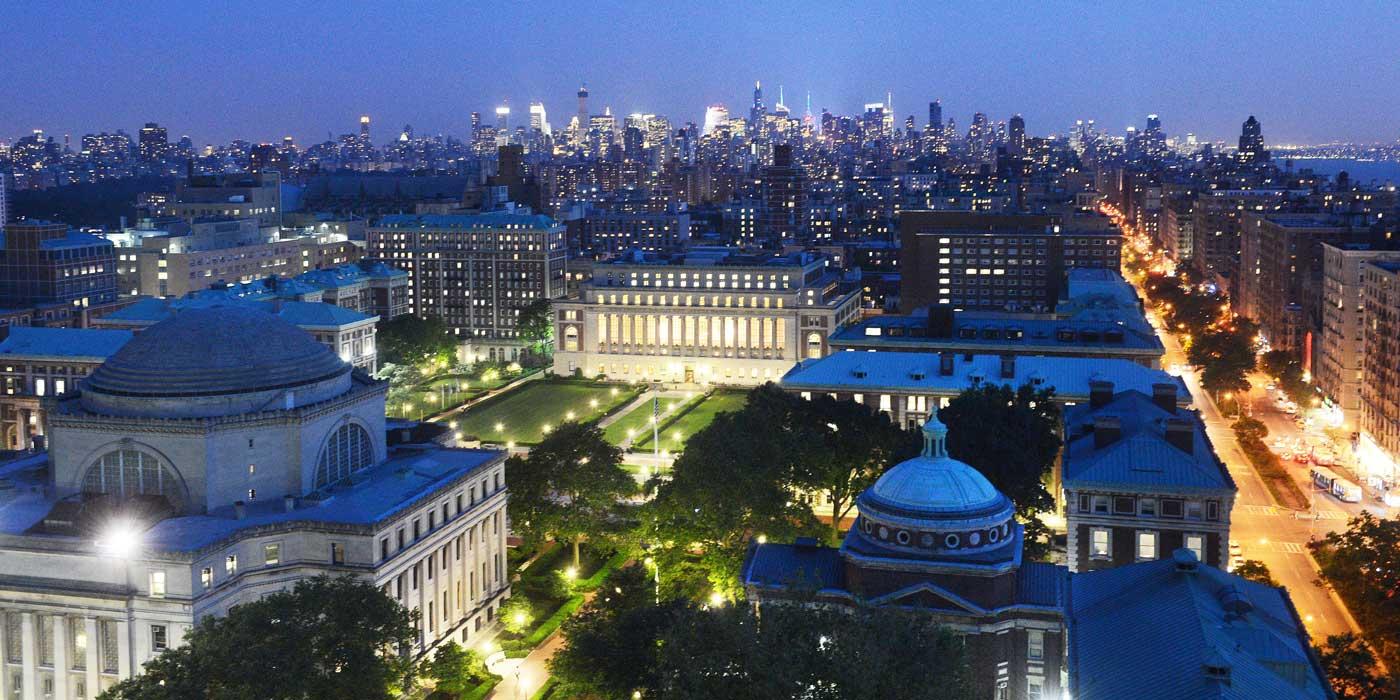 Aerial photograph of Morningside campus at night, with the NYC skyline in the background
