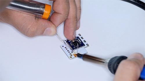 Two hands working on a microchip with a soldering iron hand tool.